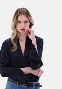 Blusa di raso navy con scollatura a V profonda, maniche ampie e una texture liscia, abbinata a jeans a vita alta e una cintura nera.
