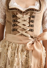 Robe traditionnelle avec un corsage beige brodé orné de dentelle, de laçage en ruban, et une jupe agrémentée de dentelle florale et d'accents en perles.