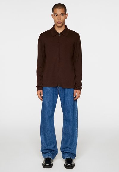 Maglione marrone con zip e colletto, abbinato a jeans a gamba larga blu chiaro e scarpe nere. Design semplice e texture liscia in tutto.