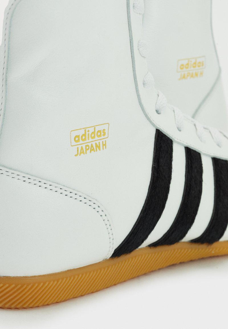 Weiße Leder-Sneaker mit schwarzen Wildlederstreifen und goldenem "adidas JAPAN H"-Logo. Die Gummisohle und die gestickten Details werten das Design auf.