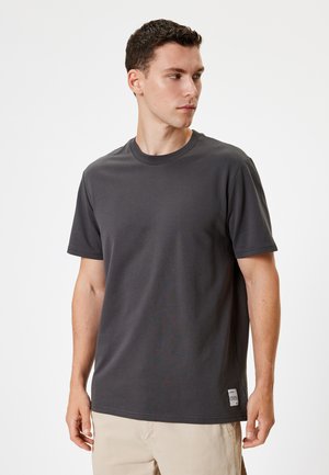 Camiseta de manga corta gris carbón hecha de algodón, con cuello redondo, corte regular y una pequeña etiqueta de logo en el dobladillo. Textura suave.