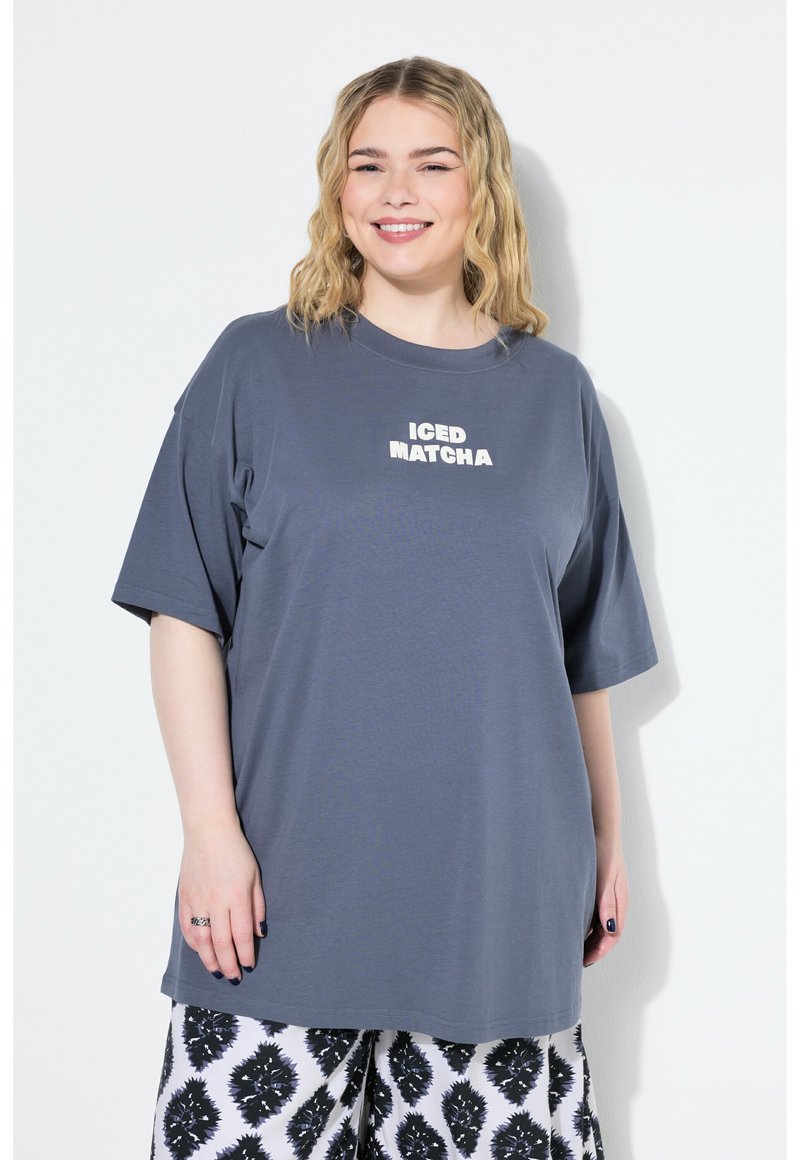 Šedé oversized tričko z měkké látky, na kterém je bílý nápis "ICED MATCHA", má krátké rukávy a uvolněný střih.