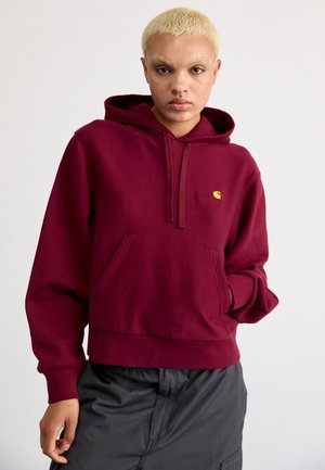Sudadera con capucha de color burdeos, con bolsillo frontal, puños y dobladillo acanalados. Presenta un pequeño logo amarillo en el pecho. Textura de tela suave.