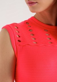 Haut ajusté à manches courtes de couleur rose vif, présentant un design découpé à motifs au niveau du col et une texture côtelée sur l'ensemble.