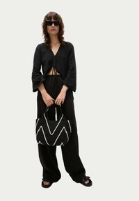 Top corto nero con dettaglio a nodi, pantaloni larghi neri e borsa a zigzag bianco e nero. Indossato con sandali neri piatti.