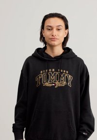 Hanorac negru din bumbac, având un logo mare aurit "TOMMY New York". Include o buzunare frontală și glugă cu șnur.
