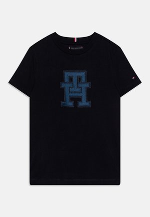 Schwarzes T-Shirt mit kurzen Ärmeln und großem blauen gestickten "TH"-Logo auf der Vorderseite sowie kleiner Tommy Hilfiger-Flagge am linken Ärmel.
