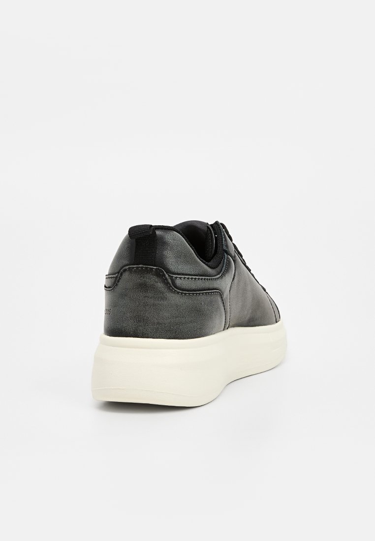 Sneaker in pelle nera con una texture liscia, forma arrotondata e suola in gomma bianca. Presenta un passante sul retro per una facile calzata.