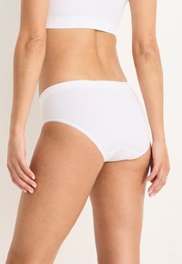 Weiße Baumwoll-Slips mit nahtlosem Design, ausgestattet mit einem weichen Bund und minimaler Abdeckung. Glatte Textur und standardmäßiger Schnitt.