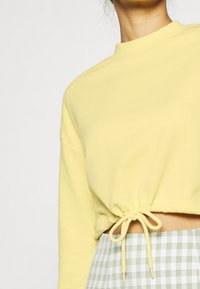 Sweat-shirt court jaune avec un col rond et un cordon froncé à la taille, assorti à un pantalon à carreaux verts et blancs.