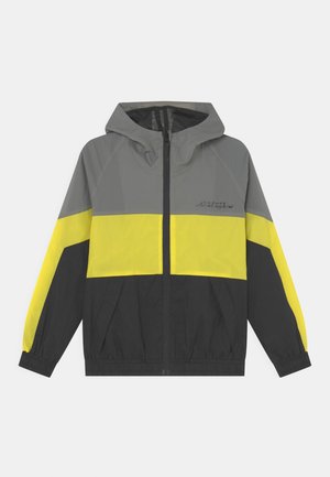 Hættetrøje vindjakke med grå øverste del, gul midterstribe, sort nederste sektion, frontlynlås og elastiske manchetter.