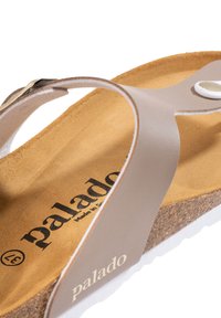 Light brown sandal with a toe loop, cork footbed, white outsole, and a small accent button. Features brand name "palado" on the insole.
