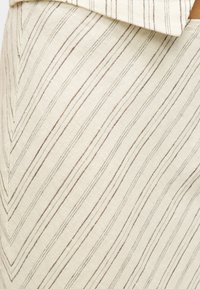 Μπεζ ύφασμα με διαγώνιες καφέ ρίγες. Η υφή φαίνεται απαλή με υφαντό σχέδιο. Ο σχεδιασμός παρουσιάζει αντίθετες γραμμές για οπτικό ενδιαφέρον.