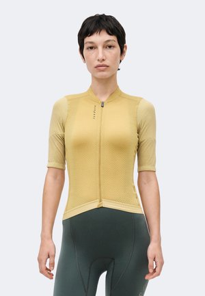 Person mit kurzen dunklen Haaren, die ein kurzes, senfgelbes Radtrikot und dunkelgraue, gepolsterte Radhosen trägt.