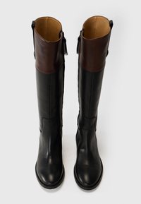 Bottes jusqu'aux genoux avec un tige en cuir noir et un dessus en cuir marron. Présente une texture lisse et une fermeture éclair latérale avec un accent en pompon.