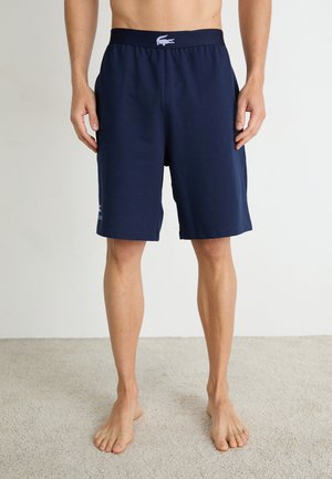 Șorturi din bumbac bleu marin, cu un tiv elastic, având un logo pe piciorul stâng și o croială lejeră. Material texturat, design până la genunchi.