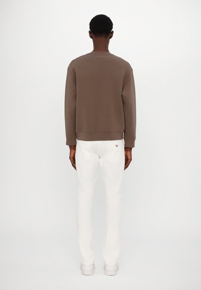 Brown sweatshirt with a crew neckline, paired with white slim-fit pants and white sneakers, viewed from the back. Smooth fabric texture.