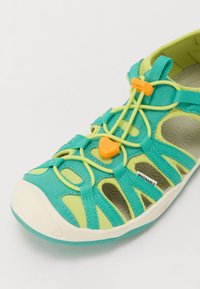 Vaskbare sandaler med en blanding av teal og limegrønt materiale, med en teksturert såle, justerbare gule snøring med toggle-lukking og utskjæringsdesign.