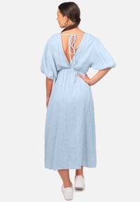 Robe bleu clair à manches bouffantes en tissu texturé, avec un détail à nouer dans le dos. La robe a un design ample et fluide jusqu'à la cheville.