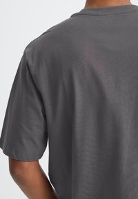 T-shirt in cotone grigio con maniche corte, caratterizzato da un collo rotondo e una texture morbida. Cuciture visibili lungo l'orlo e le maniche.