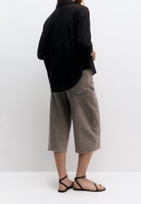 Chemise noire à texture, culottes en denim gris lâches avec bords effilochés, et sandales plates noires avec brides autour de la cheville. Design minimaliste.