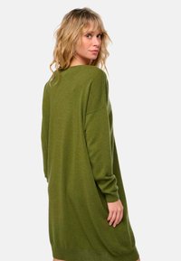 Robe pull oversize vert olive avec des manches longues, des poignets côtelés et un décolleté en forme de scoop. Tissu doux et texturé qui tombe de manière fluide.