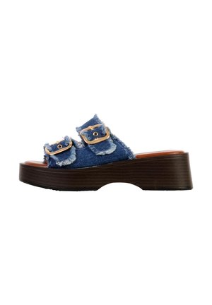 Sandale plateforme avec semelle marron foncé et brides en denim effilochées, chacune avec une boucle dorée, vue latérale sur fond blanc.