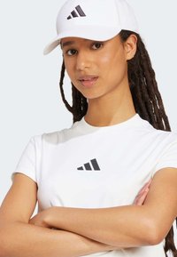 Balta īsām piedurknēm T-kreklu ar melnu adidas logo uz krūtīm, apvienojot to ar balta cepuri, kurai ir tas pats melnais logo.