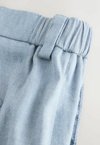 Ceinture de pantalon en jean bleu clair avec dos élastique et passants de ceinture, montrant la texture du tissu et les détails des coutures.