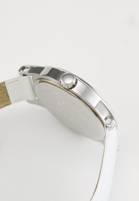 Orologio in metallo argento con cassa rotonda, cinturino in pelle bianca e corona argentata con texture. Retro liscio con dettagli incisi.