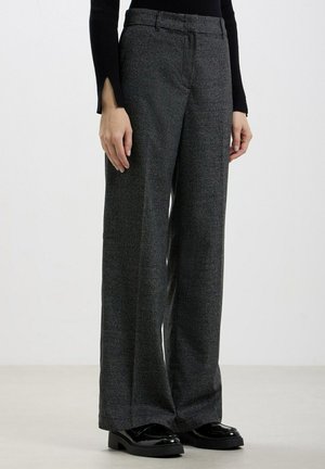 Pantalons larges en tissu texturé gris foncé, dotés d'une taille haute, de passants de ceinture et d'un motif à carreaux subtil. Mocassins noirs brillants.