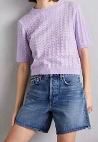 Liliowy dzianinowy top z krótkimi rękawami i fakturowanym wzorem; w połączeniu z wysokim stanem jeansowych szortów w jasnoniebieskim kolorze z postrzępionymi krawędziami.