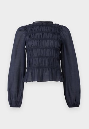 Blouse bleu marine semi-transparent avec un corsage smocké, des manches longues et un ourlet volanté. Présente une texture froncée sur l'ensemble.