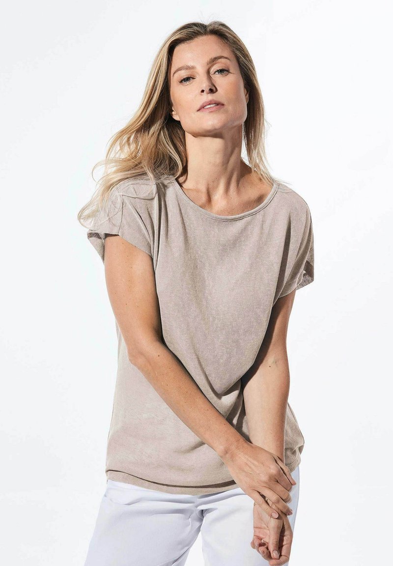 Lichte taupe T-shirt met een relaxte pasvorm, ronde halslijn en opgerolde korte mouwen, gemaakt van zachte stof, gecombineerd met witte broeken.