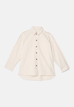 Chemise crème à manches longues en tissu doux, dotée d'un col, d'une poche poitrine et de boutons marron sur le devant.