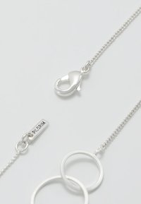 Collar de cadena de plata que presenta un cierre de langosta, dos anillos interconectados y una etiqueta grabada con "PILGRIM". Acabado suave y eslabones delicados.