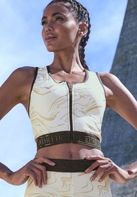 White sports bra with gold marble pattern, zip front, and wide black band featuring the text "ATHLETIC" embossed in gold.