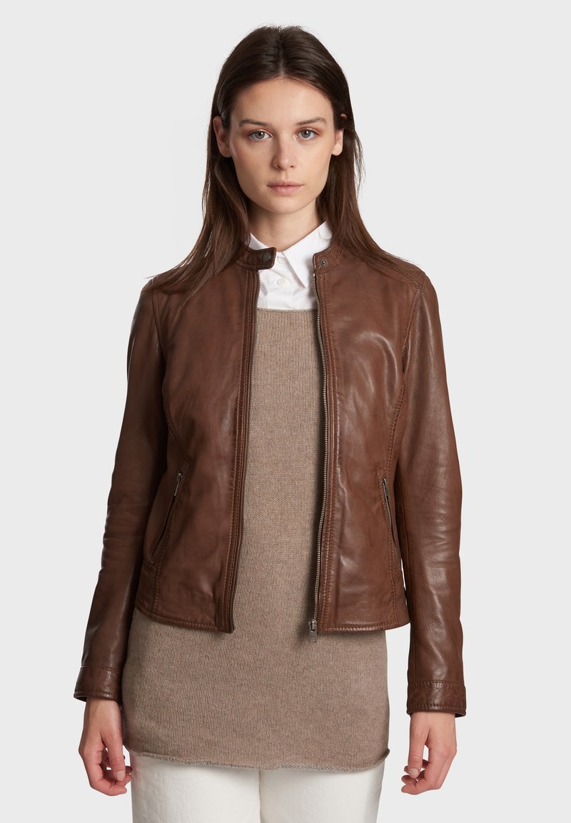 Bruine leren jack met een rits aan de voorkant, slim fit en een ronde kraag. Gelaagd over een beige trui. Soepele textuur en op maat gemaakt ontwerp.