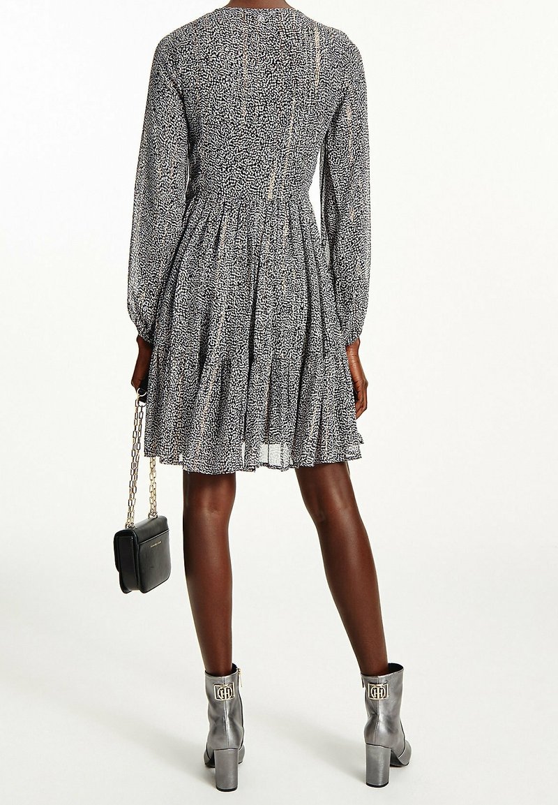 Robe imprimée noir et blanc avec manches longues, jupe plissée et fermeture à boutons dans le dos. Associée à des bottines grises et un petit sac noir.