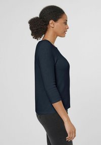 Dunkelblauer Pullover mit Rundhalsausschnitt und 3/4-Ärmeln, aus einem weichen, glatten Material, kombiniert mit schwarzen Hosen.