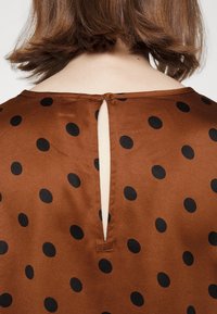 Tissu en satin marron à pois noirs sur le dos d'un chemisier, avec une petite ouverture en forme de goutte d'eau et de courts cheveux marron au-dessus de la nuque.