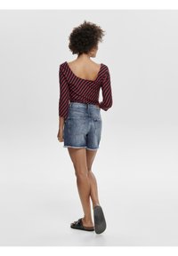 Rote und schwarze gestreifte Langarmbluse mit einem runden Rückenausschnitt, kombiniert mit Jeansshorts mit fransigem Saum und zwei Gesäßtaschen.