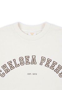 Biała bluza z brązowym łukowym napisem "CHELSEA PEERS" oraz "EST. 2012." Ribnowany okrągły dekolt i miękka tekstura z minimalnym wzorem.