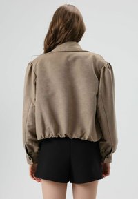 Brown puff-sleeve jacket with a cinched hem and buttoned cuffs, made of smooth fabric. Worn over black shorts.