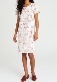 Kurzärmliges Blumenkleid in Weiß mit pinkfarbenen Mustern, knielang, aus leichtem Stoff, kombiniert mit rotbraunen Mokassins.