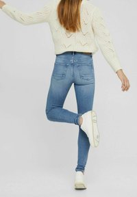 Jeans skinnies azul claro con un lavado medio, que presentan una silueta ajustada, cinco bolsillos y detalles de costura, combinados con zapatillas blancas.