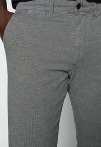 Šedé texturované kalhoty slim fit s knoflíkovým uzávěrem v pase a bočními kapsami. Viditelné švy vylepšují design.