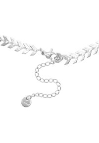 Bracciale in metallo argento con maglie a zigzag interconnesse, chiusura a moschettone e catena di estensione regolabile con un'etichetta rotonda.