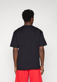 T-shirt preta de manga curta com decote redondo, feita de tecido suave. A vista traseira não mostra gráficos, com um corte descontraído e bainha padrão.