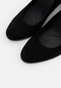 Escarpins en daim noir avec un bout arrondi, un dessus bas et une doublure intérieure lisse avec des détails perforés pour la respirabilité.